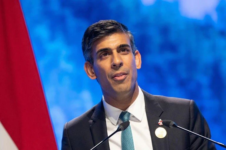 A man in a suit with a white and red flag and blue background.
