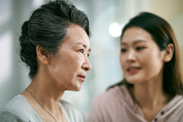 An older Chinese woman with a younger woman in the background, speaking to her