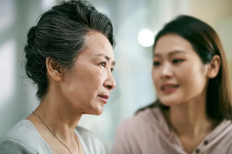 Uma chinesa mais velha com uma chinesa mis jovem ao fundo, falando com ela