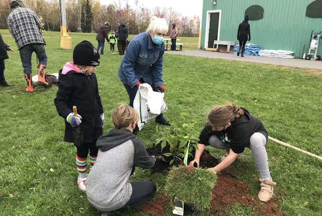 Students seen holding a seedling and grass sod outdoors.