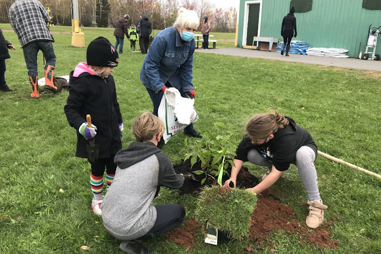 Students seen holding a seedling and grass sod outdoors.