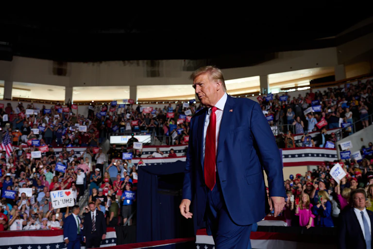 A white man dressed in a business suit is walking on a stage in front of a crowd of people.