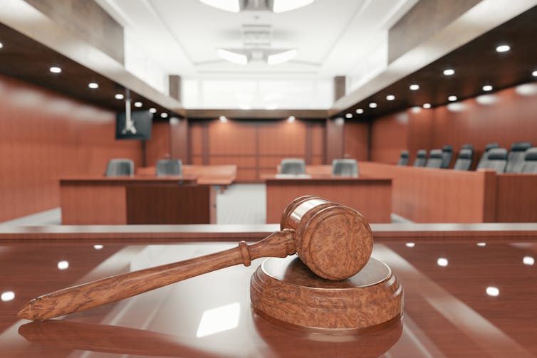 A gavel sits on a bare table, in front of an empty courtroom.