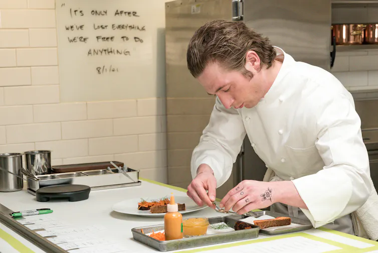 Un chef vêtu de blanc ajoute soigneusement les éléments d’un repas à une assiette