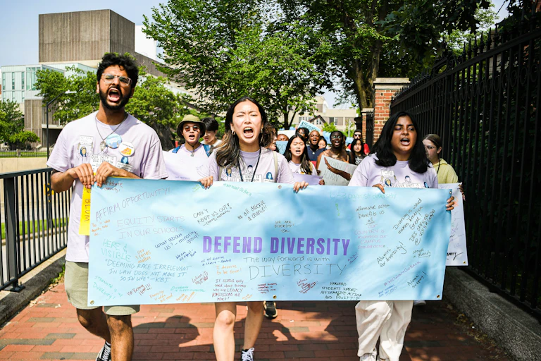 A group of protestors are marching and holding a sign that defends diversity.