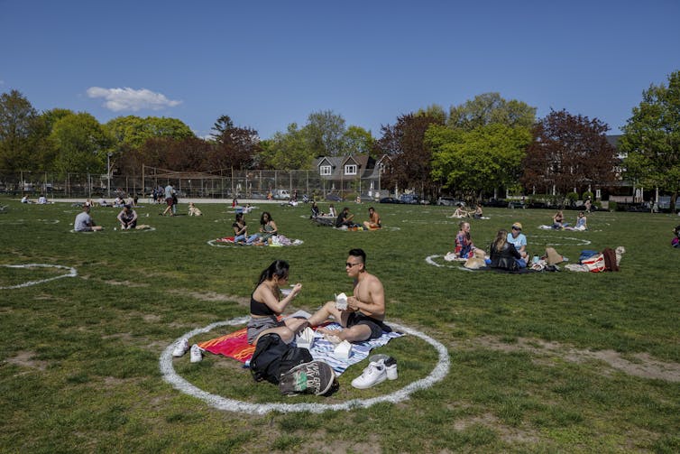 People on the grass in a large park, sitting in white circles drawn on the grass to keep people socially distanced