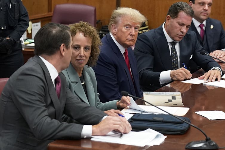 A blond man sits glowering in a courtroom.