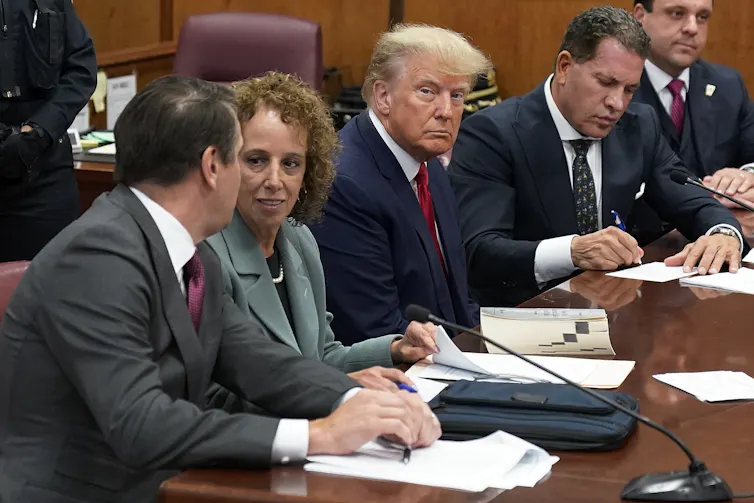 A blond man sits glowering in a courtroom.