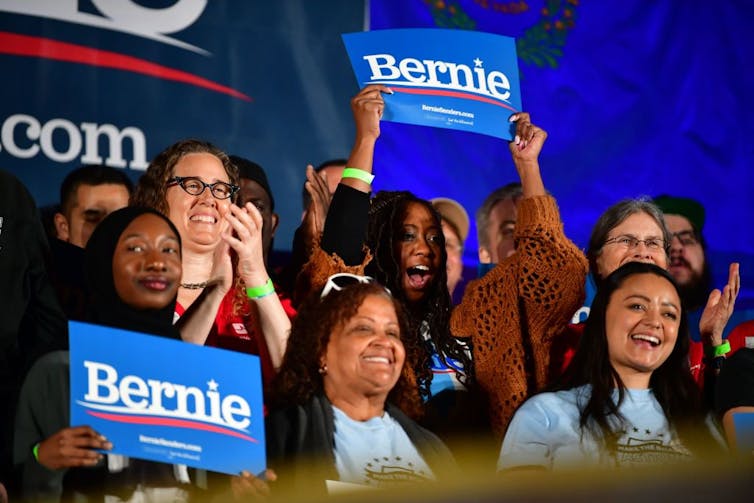 Women clap and hold blue 'Bernie' signs.