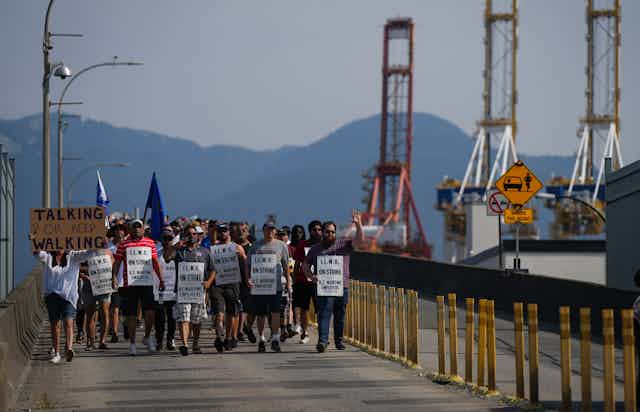 A group of people holding picket signs walk past a port