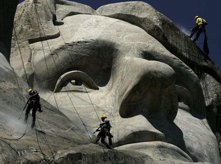 Workers clean the face of a large rock sculpture.