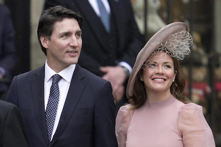 A dark haired man in a black suit and a smiling woman in a pink dress and hat.