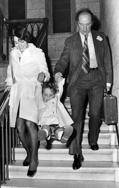A black and white photo shows an older man and a young woman swinging smiling boy between them.