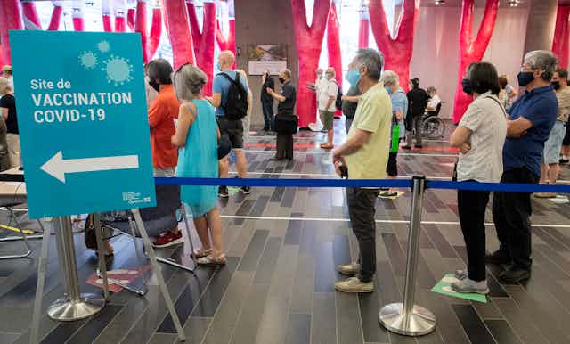 People lined up several feet apart behind a sign for a COVID-19 vaccination clinic 