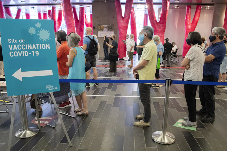 People lined up several feet apart behind a sign for a COVID-19 vaccination clinic