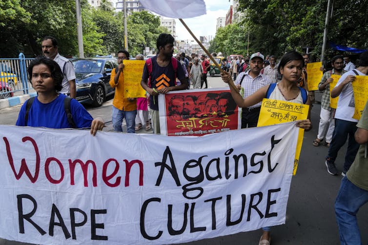 A group of people at a protest carry a banner that reads: Women against rape culture.