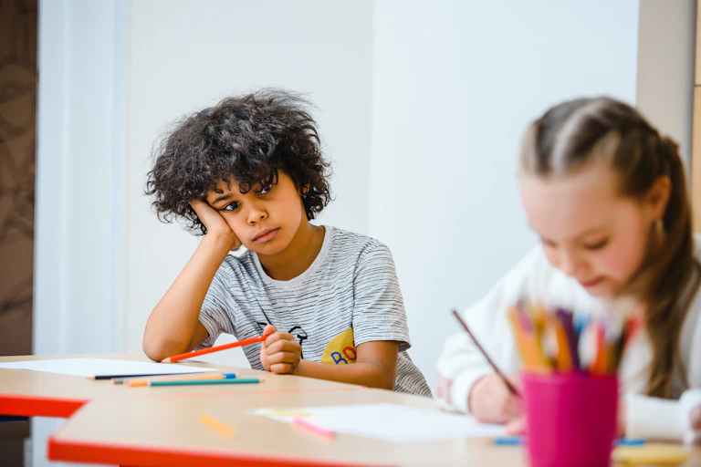 A child sits with his head in his hands. Another child works nearby.