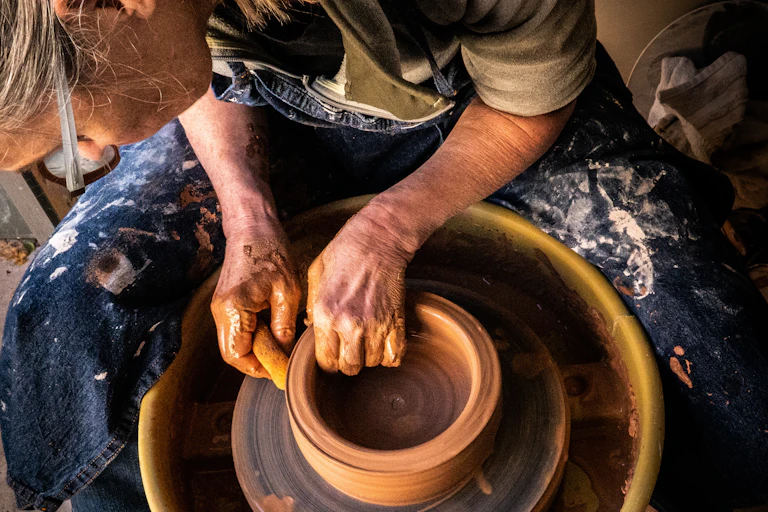 person in blue denim jeans making clay pot