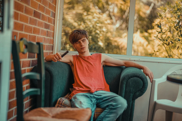 Teen sits on couch chair, vaping