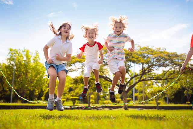 Tres niños saltan a la comba en un parque.