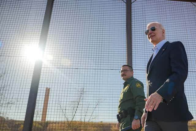 President Joe Biden walks past a high fence at the US/Mexico border.