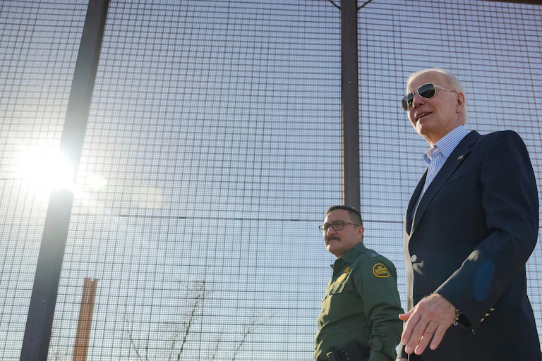 President Joe Biden walks past a high fence at the US/Mexico border.