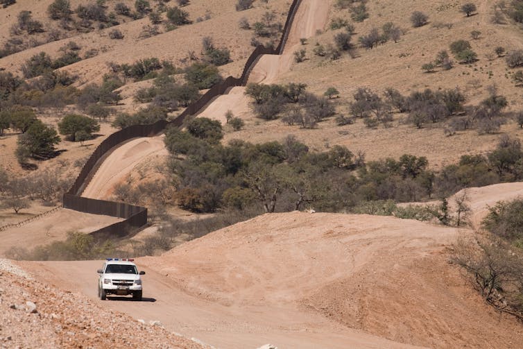 A border patrol vehicle drives along the US/Mexico border fence.