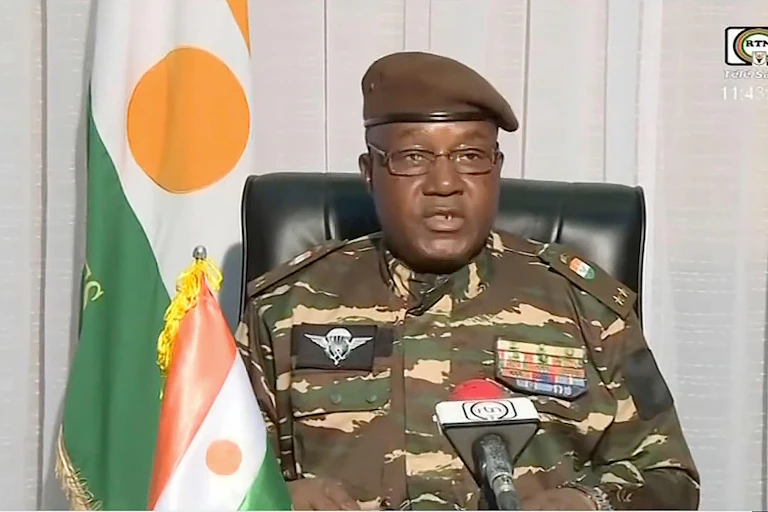 Niger coup leader Gen. Abdourahmane Tchiani in military uniform flanked by the country's flag.