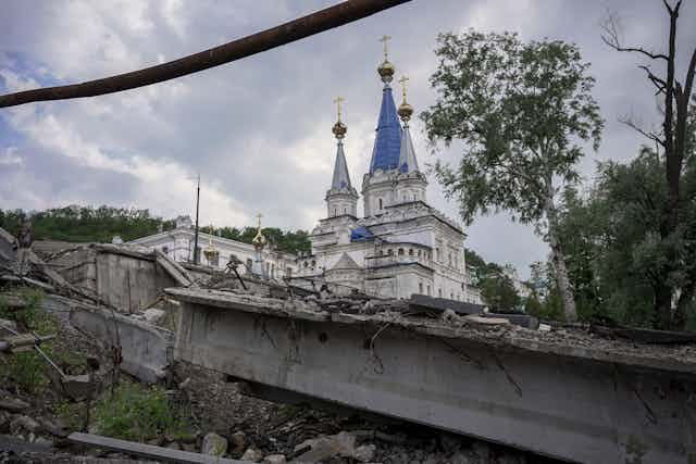 A destroyed bridge seen near a monastery, which is covered in bullet holes and fragments of shrapnel. The ruined town of Sviatohirsk in Ukraine's Donbas region.
