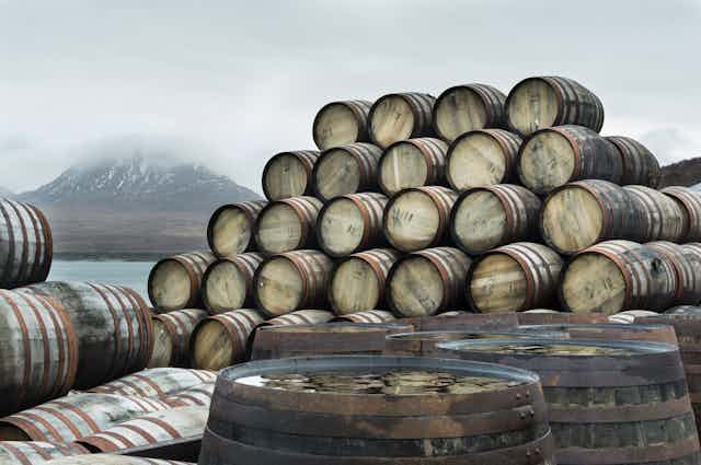 A stack of casks or barrels in front of a snow-capped mountain and cloudy sky.