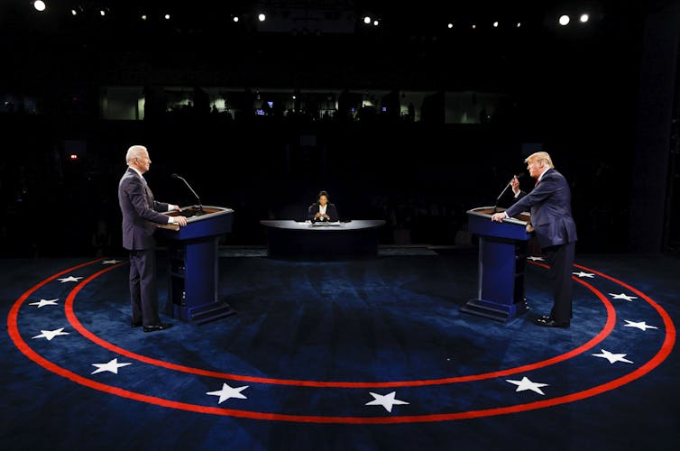 Two men are seen arguing on a large stage from behind their respective podiums.