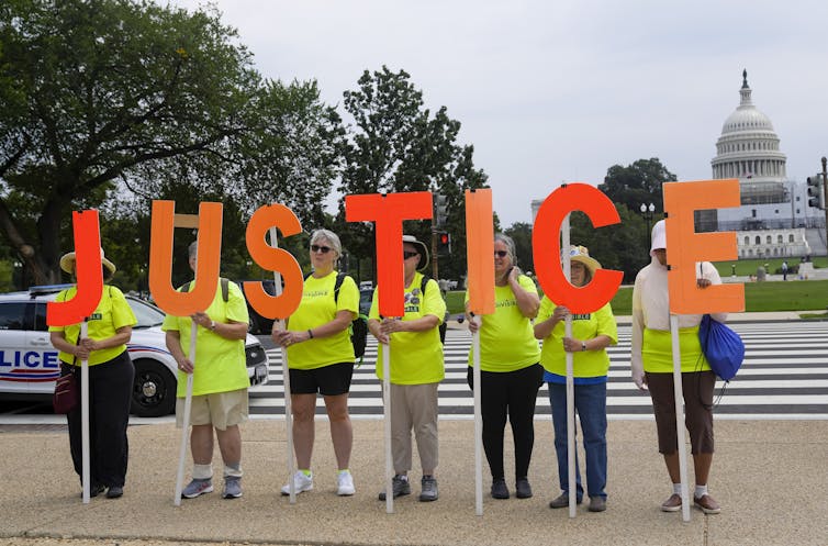 Seven protesters in neon yellow T-shirts hold orange letters that spell out 'justice.'