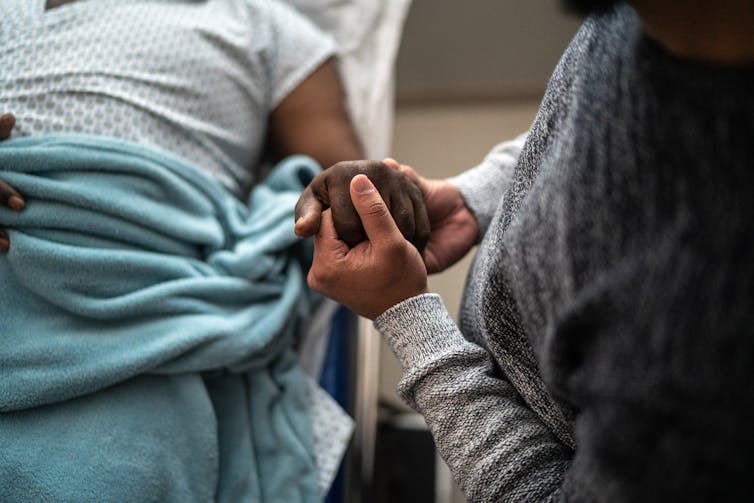 Person holding hand of patient lying in hospital bed
