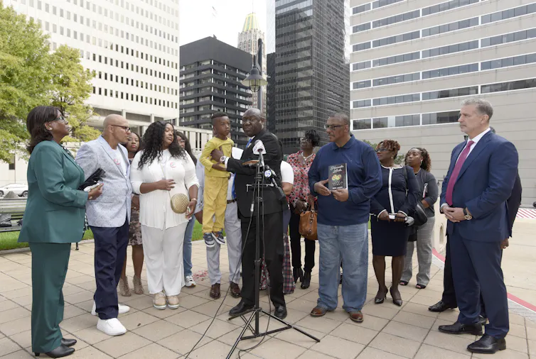 A man standing a microphone holding a child, surrounded by a group of people.
