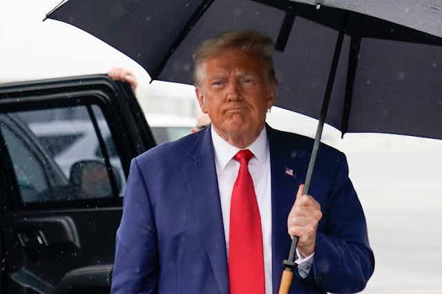 Donald Trump carries an umbrella in his left hand as he walks toward media cameras.