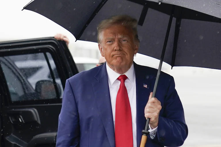 Donald Trump carries an umbrella in his left hand as he walks toward media cameras.
