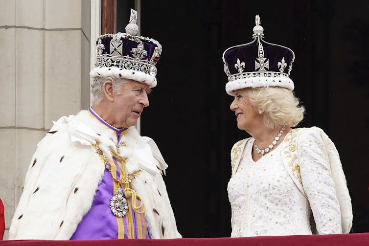 A man and woman wearing crowns and robes look at eachother