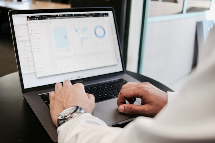 Hands using laptop showing blurred spreadsheet and graphs