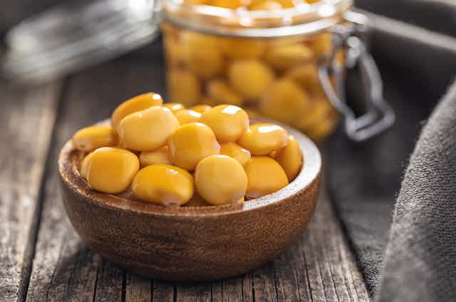 A photo shows a bowl of pale yellowish beans on a table, with a jar containing more in the background.
