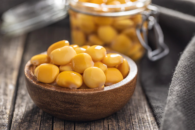 A photo shows a bowl of pale yellowish beans on a table, with a jar containing more in the background.