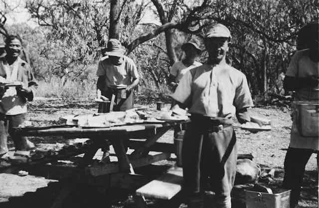 Four men stand around a picnic table.