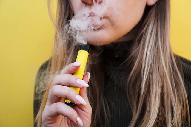 Young woman smoking vape, exhaling smoke