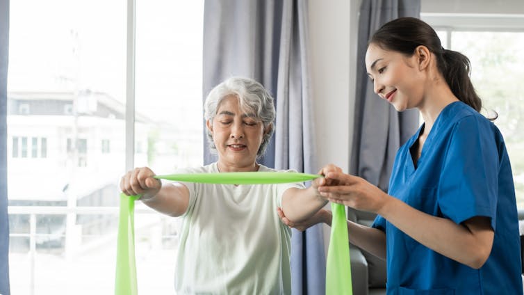A young female nurse helps an older patient perform an exercises using a resistance band.