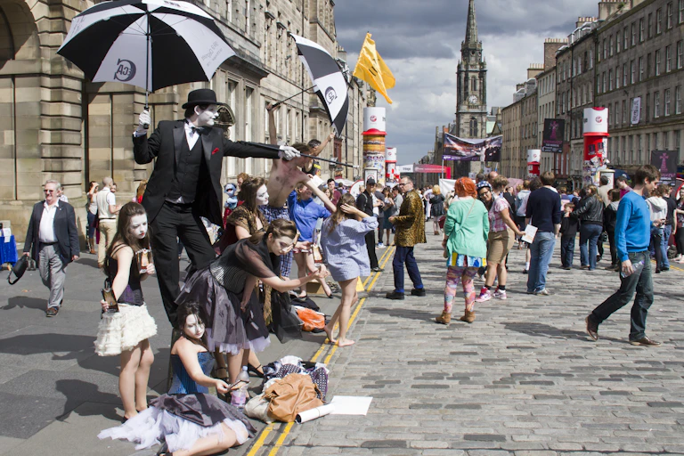 A street scene of performers, spectators and tourists milling about.