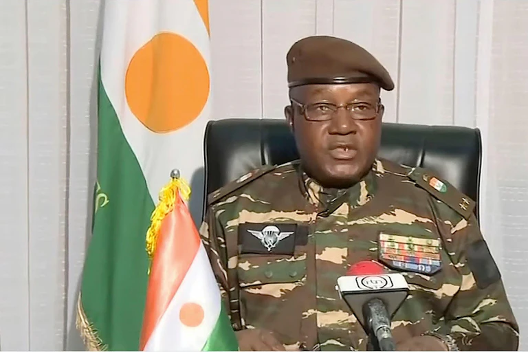 El general Abdourahmane Tchiani, líder golpista de Níger, con uniforme militar y flanqueado por la bandera del país.