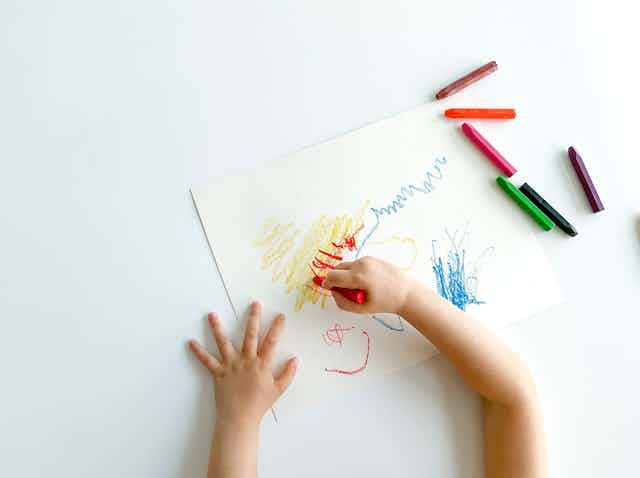 Dos manos infantiles dibujan garabatos en un folio en blanco.