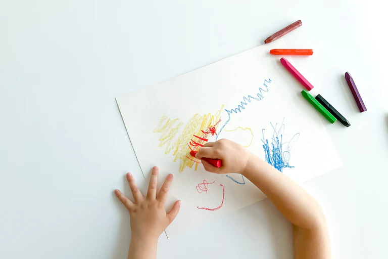 Dos manos infantiles dibujan garabatos en un folio en blanco.