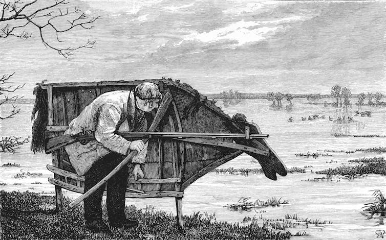 Man crouches behind wooden screen of a horse while he holds a gun