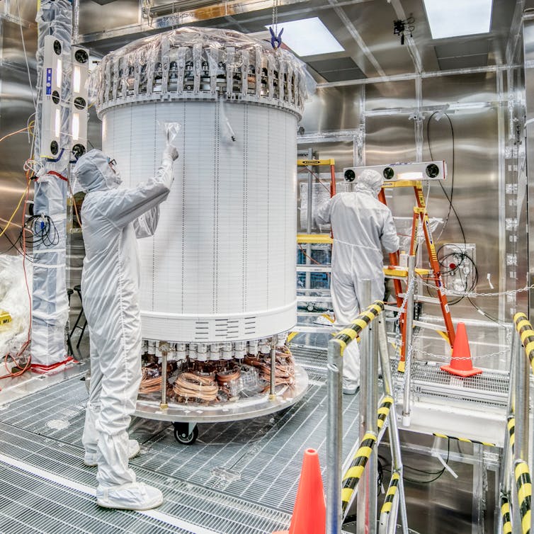 An LZ worker wearing a white hazard suit stands by a tall white cylinder.