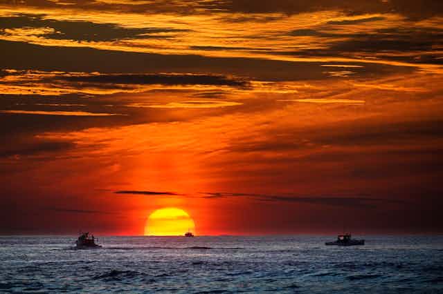Soleil se couchant sur l'océan Atlantique avec des bateaux au premier plan.
